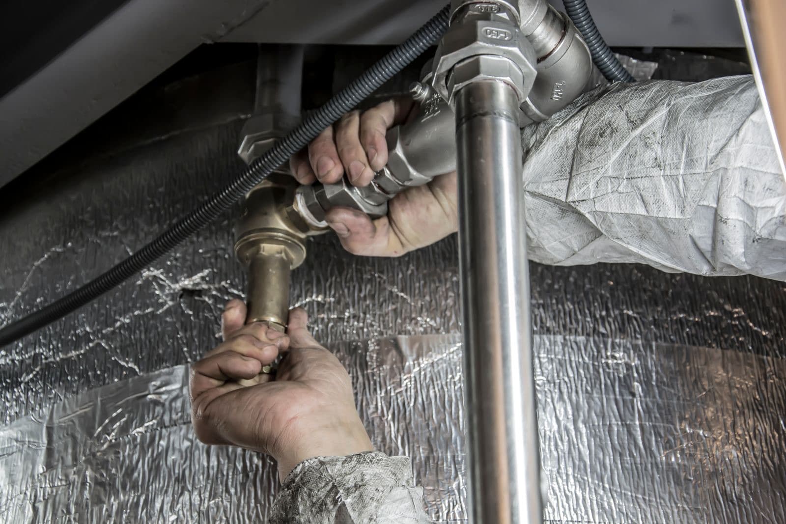 Stock photograph of plumbing work on a metal pipe connection beside insulated pipework.