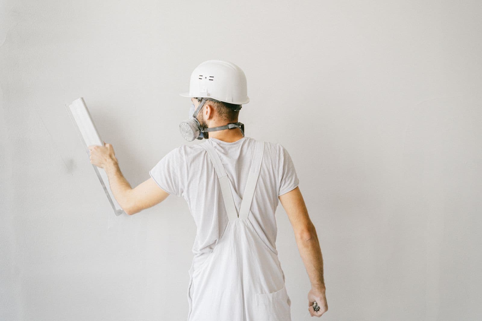 Repairing a wall before repainting: a decorator in white overalls preparing a plastered wall for paint